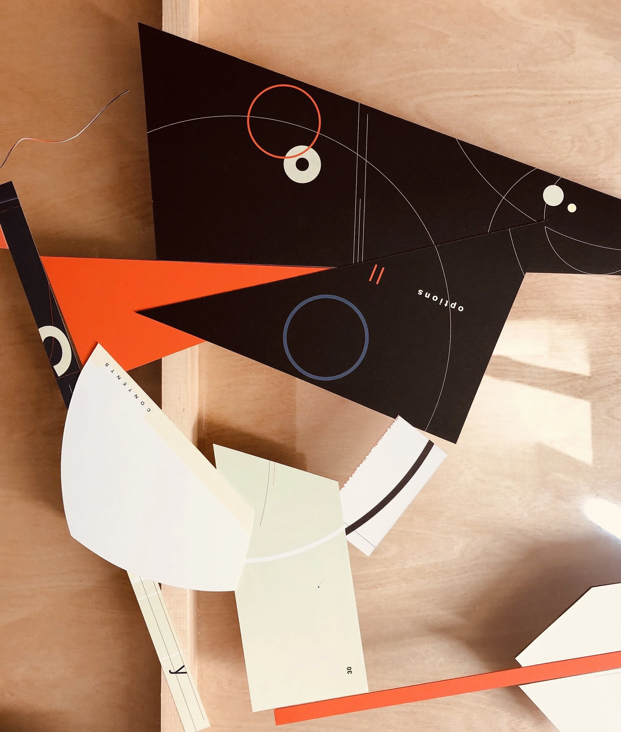 Colorful abstract art and geometric shapes on paper, including circles, lines, and text, resting on a wooden surface.