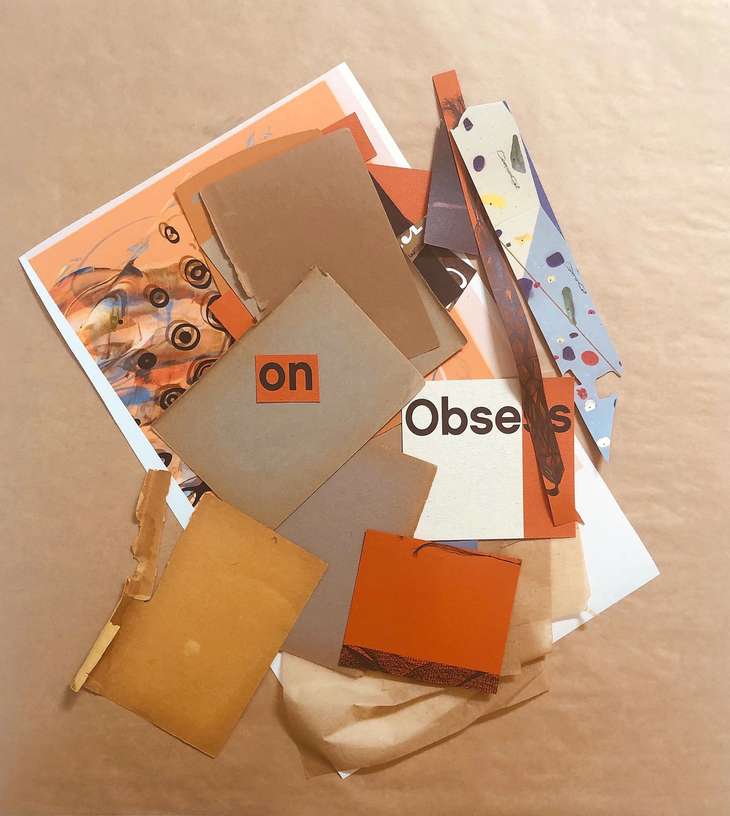 A pile of cut-out paper pieces with various colors and patterns, some with text like 'on' and 'Obses' on a beige background.