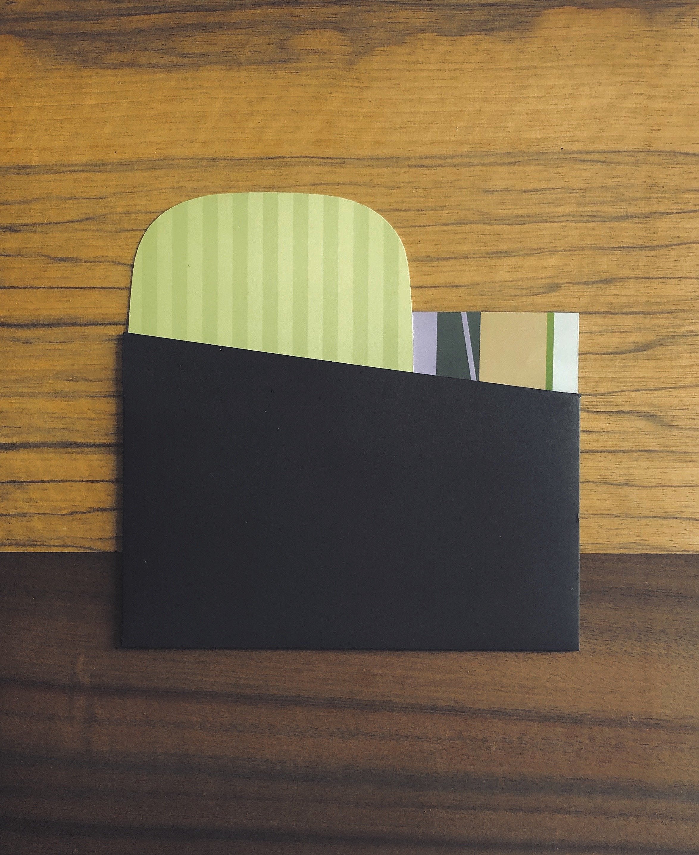 A black envelope partially opened, revealing several thank you cards inside, placed on a wooden surface.