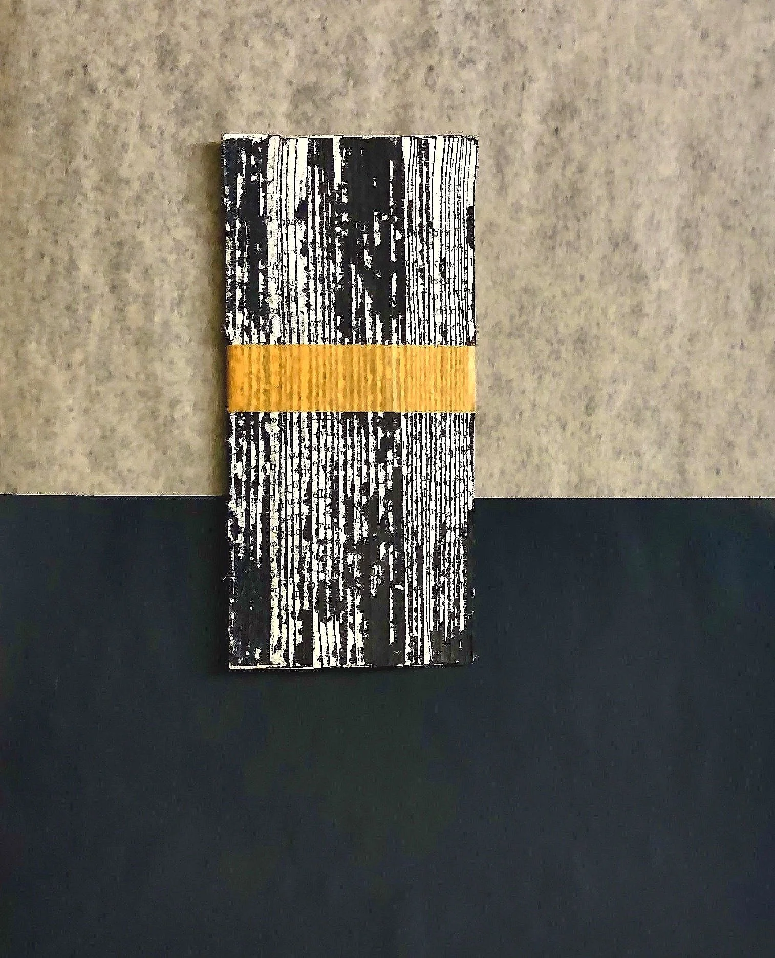 A rectangular wooden block painted with black and white stripes, with a yellow band across the middle, placed on a surface with a two-tone background.