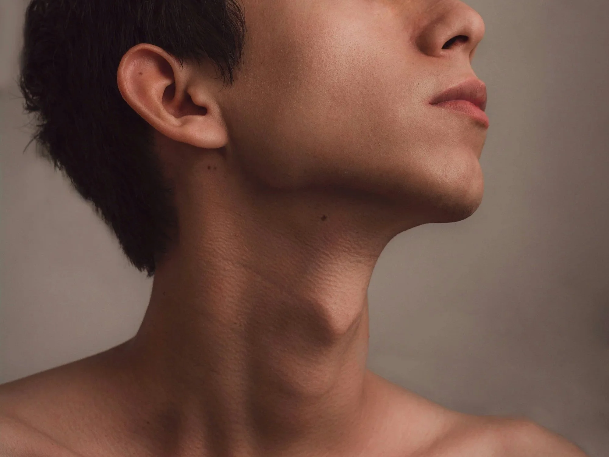 Close-up of a person's face and neck in profile, with smooth skin, short dark hair, and neutral background.