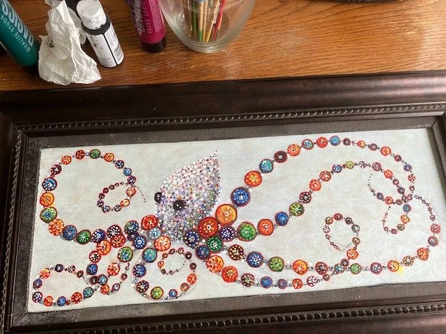 A new painting by John Cayden of a beautiful multi-colored cephalopod in the Tlingit and Haida animal art style , displayed on a table with painting supplies around it.