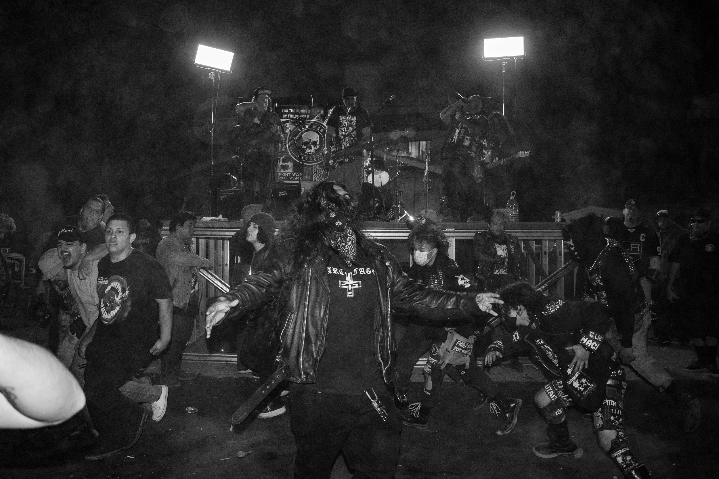 People dancing and enjoying a live music concert at night with a band performing on stage in the background.