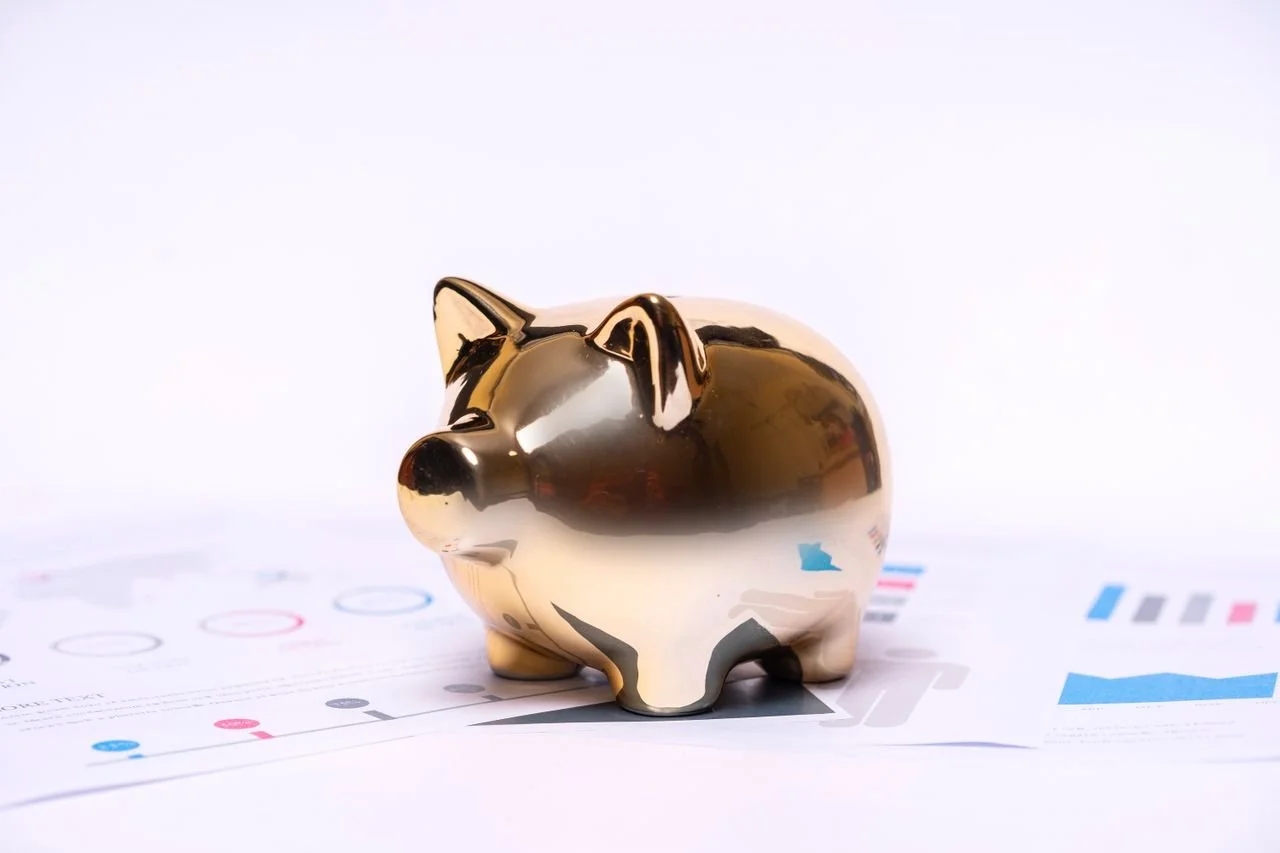 A shiny, gold and black piggy bank sitting on a desk with printed charts and graphs underneath, with a plain white background.