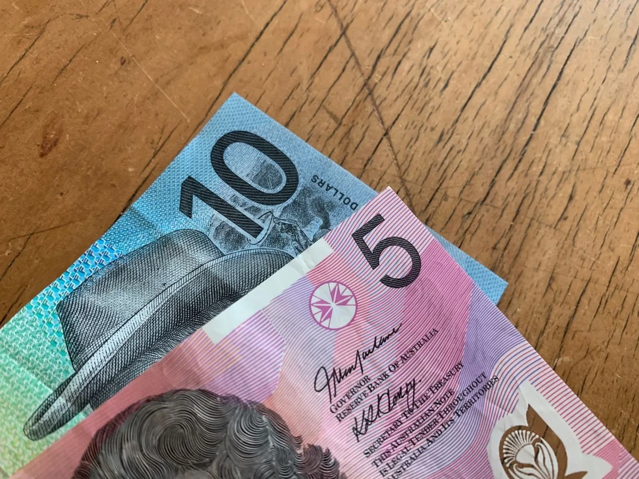 Close-up of an Australian 10-dollar banknote and a 5-dollar banknote on a wooden surface.