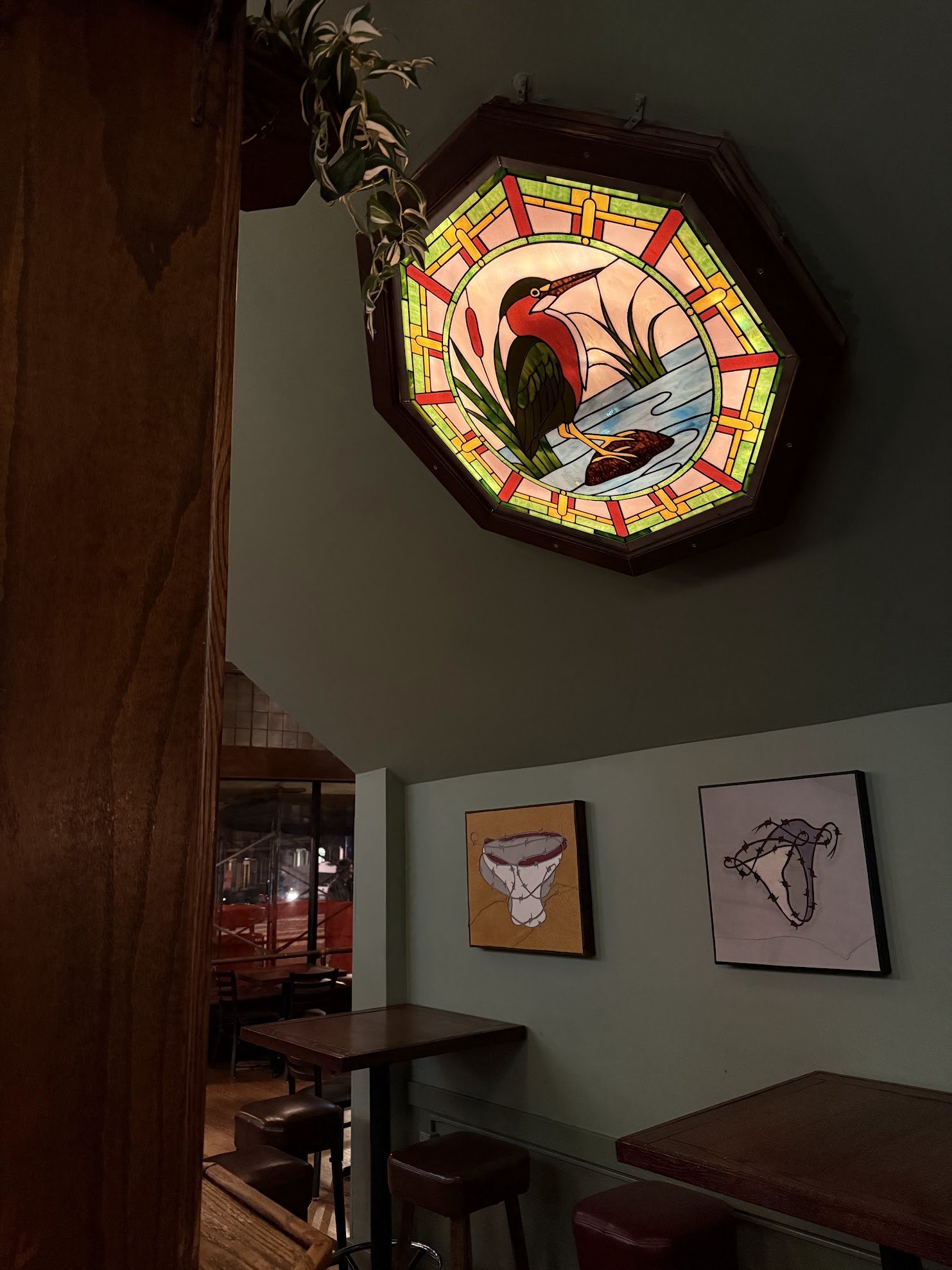 stained glass of a bird and art pieces by a local artist near high top tables in a bar setting