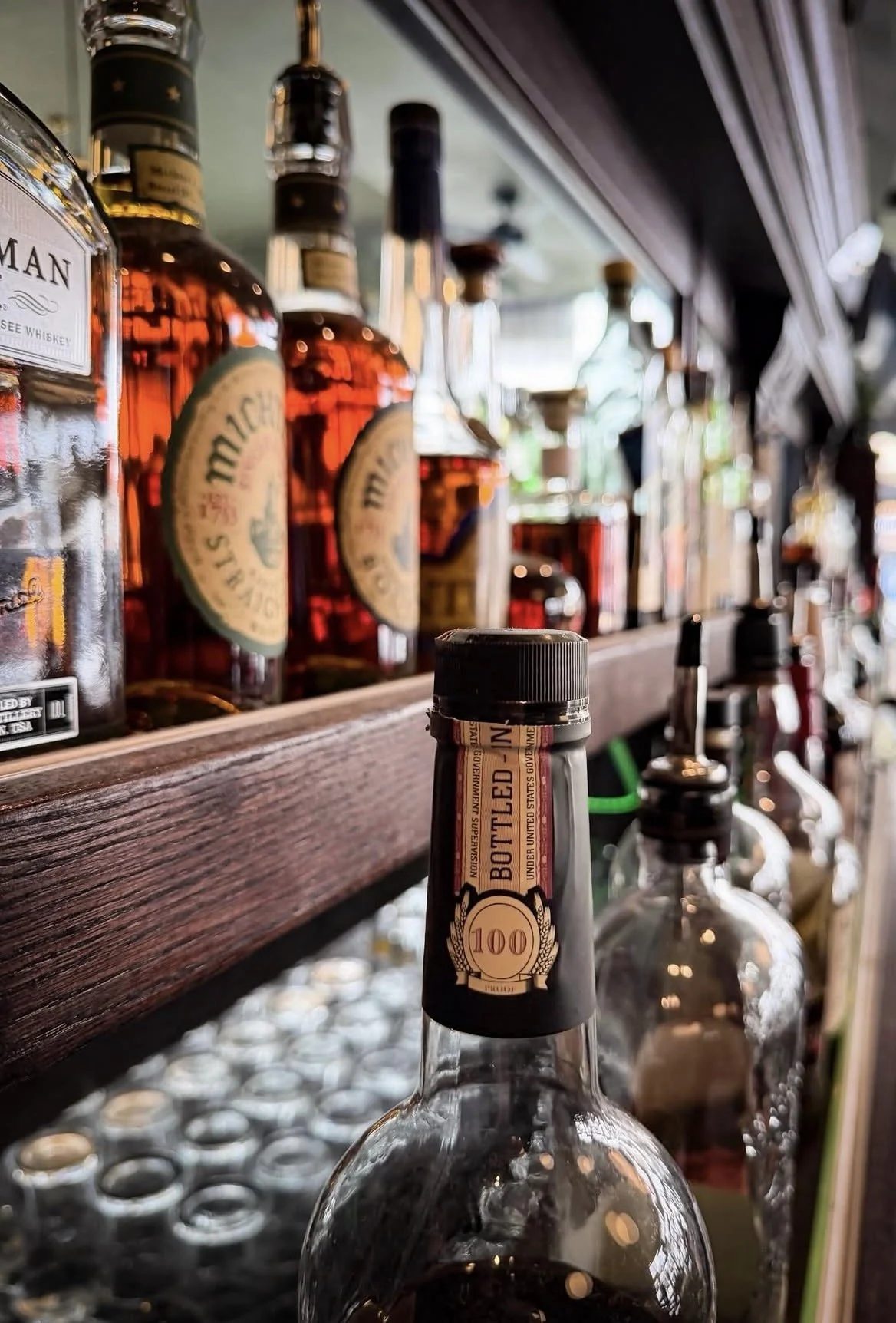 View of liquor bottles, including Jack Daniel's whiskey, on a bar shelf with a focus on an empty bottle in the foreground.