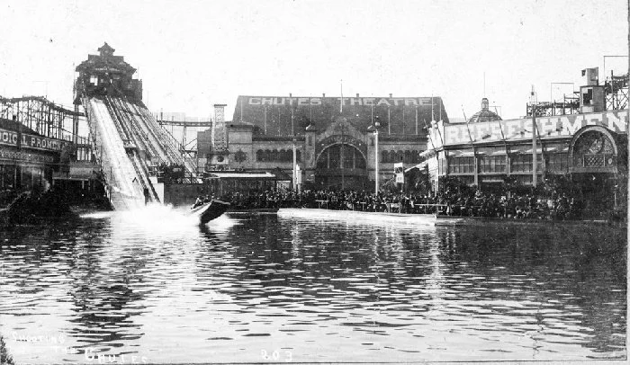 A boat splashes into the lake in front of the large Chutes Theatre and Refreshments buildings, around 1900.