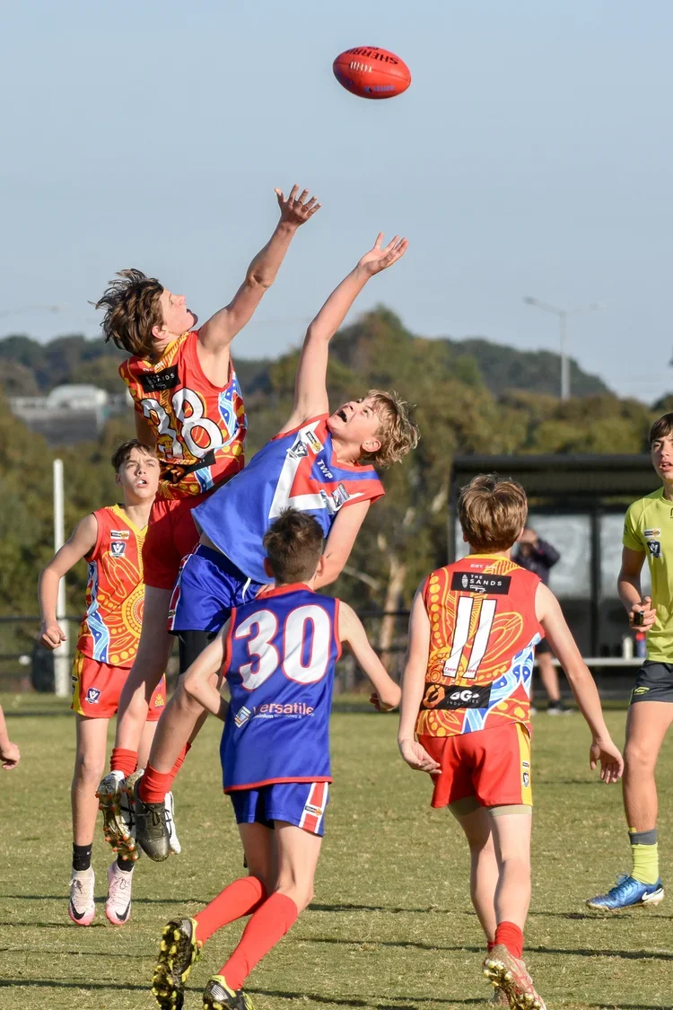 Children playing Australian rules football outdoors, jumping to catch a ball in the air.