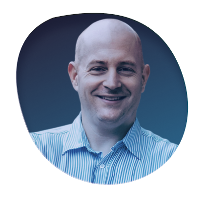 Smiling bald man in a blue striped shirt in front of a blurred background.