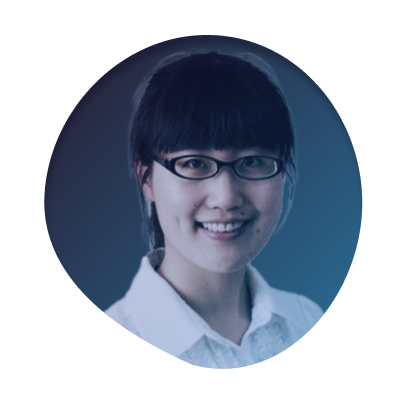 A woman with black hair and glasses smiling against a blue background.