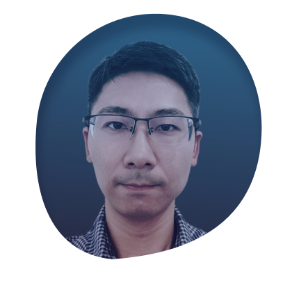 Close-up portrait of a young man with short black hair, wearing glasses, and a blue checkered shirt, against a light background.