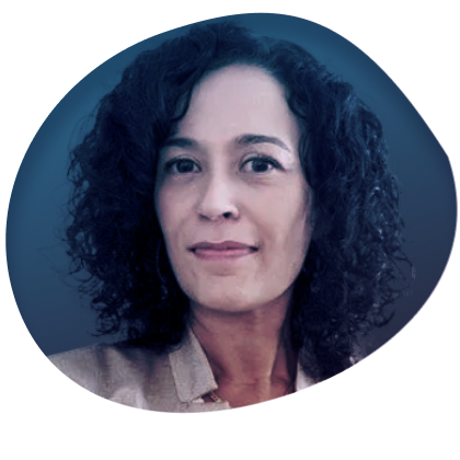 A woman with curly dark hair looking at the camera, wearing a light-colored blazer against a plain background.
