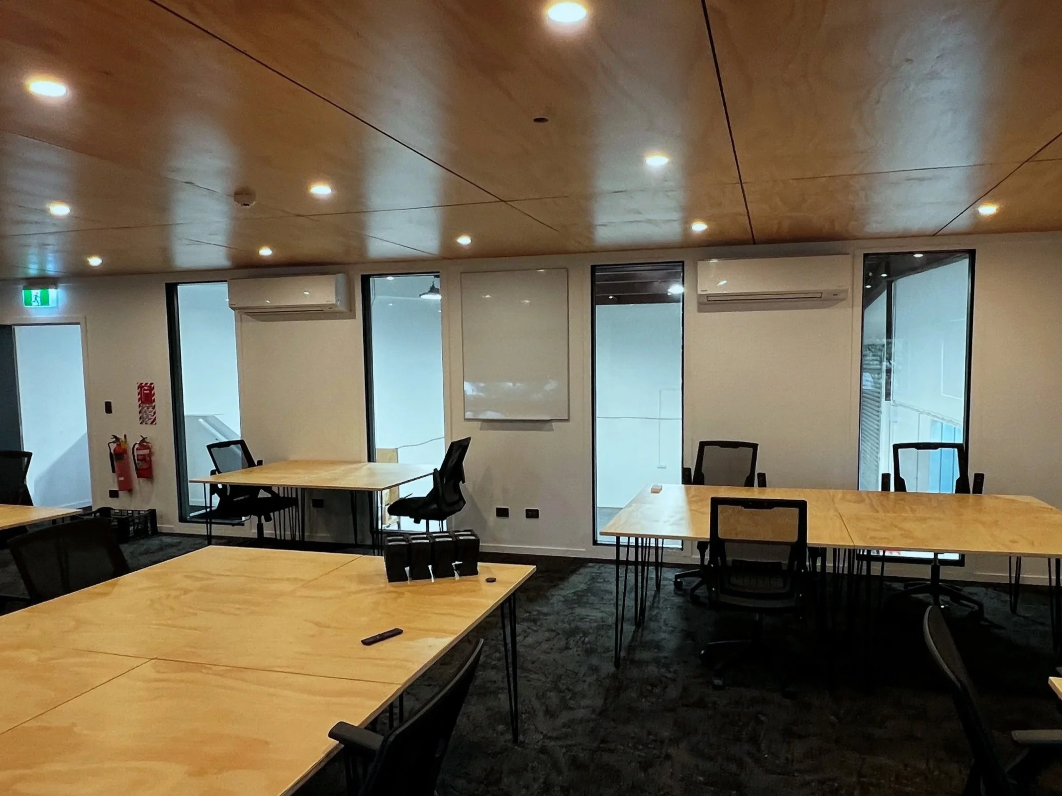 Production offices, Event spaceor Conference room with wooden tables, black office chairs, large windows overlooking the warehouse, and wooden ceiling with recessed lighting.