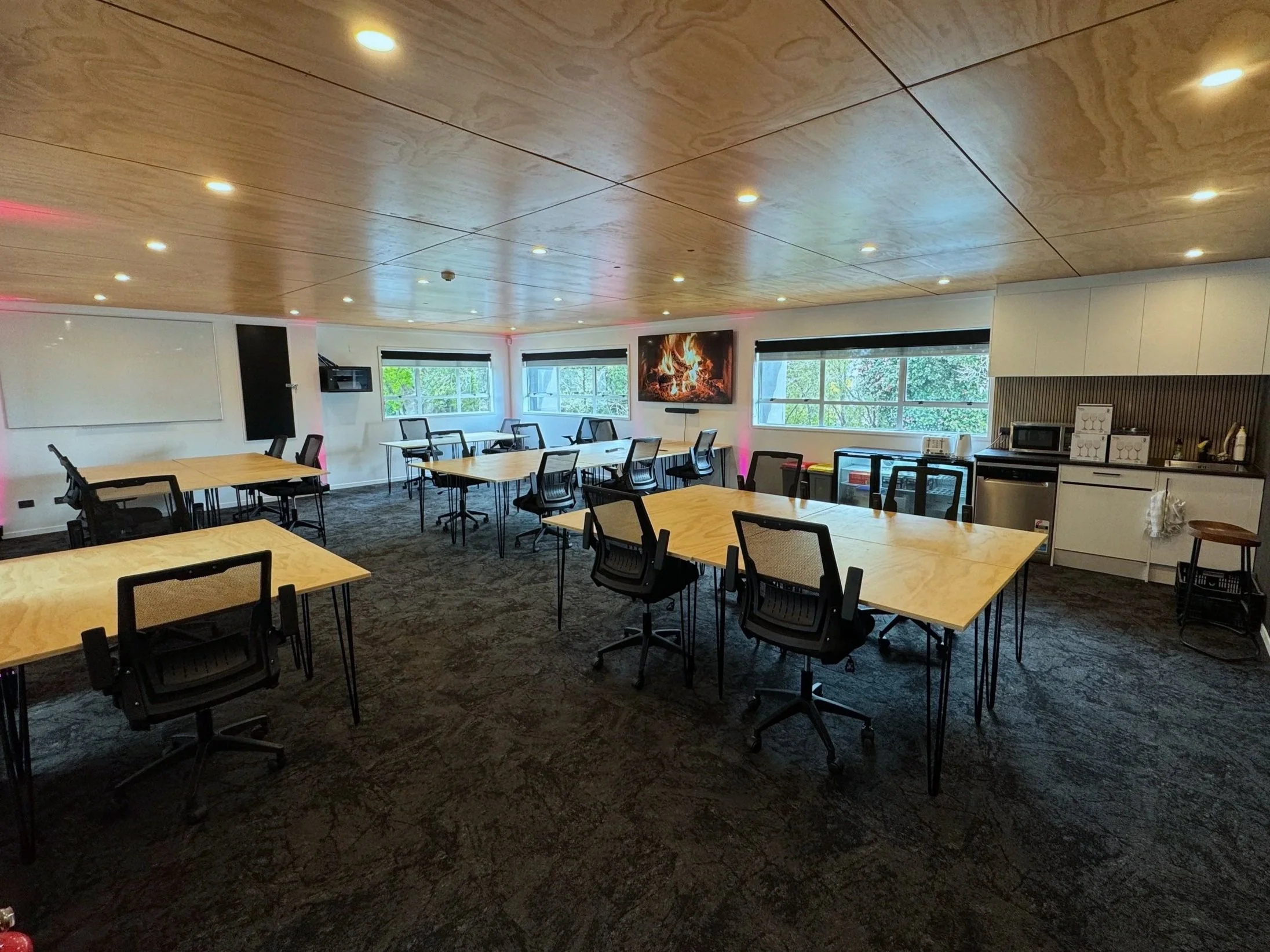 Production offices, Event space or Conference room with wooden tables, black office chairs, a whiteboard, a wall-mounted TV, and kitchenette.