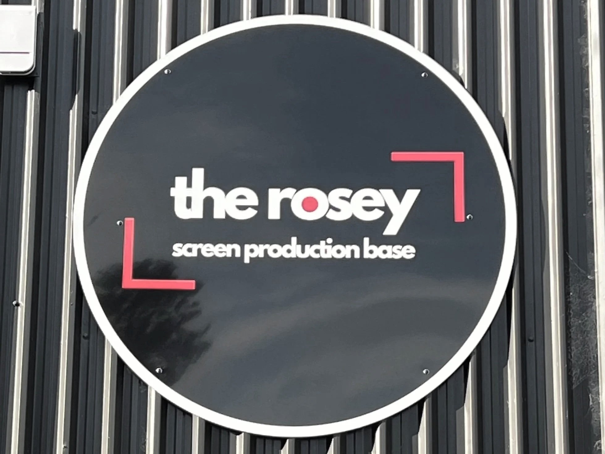 Sign for the Rosey screen production base with white text on a dark background and red corner accents.
