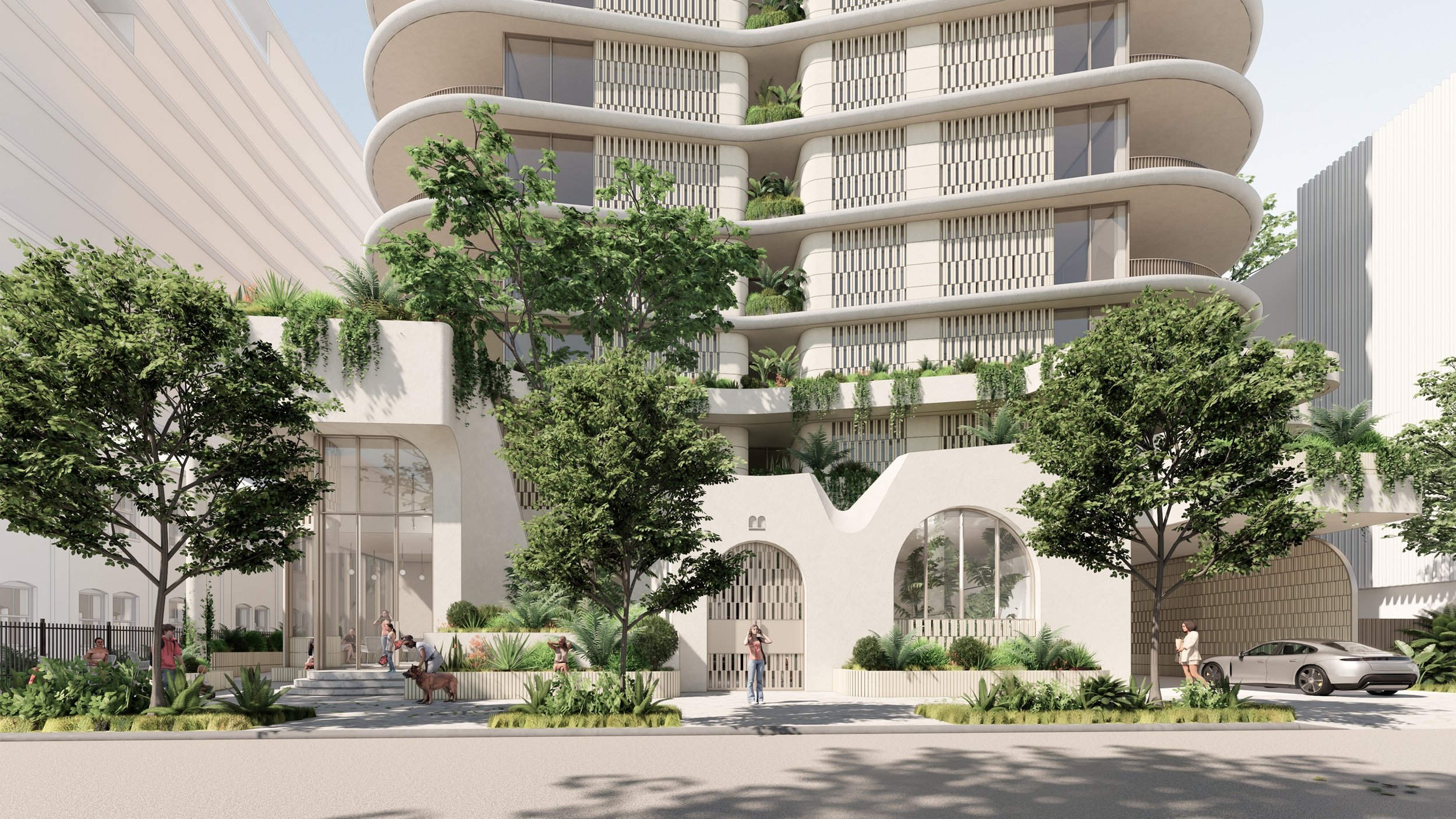 Aerial view of modern multi-story apartment building with balconies, surrounding houses, and a sports field in the distance on a sunny day.