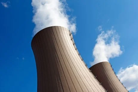 Cooling towers emitting steam against a blue sky with clouds.
