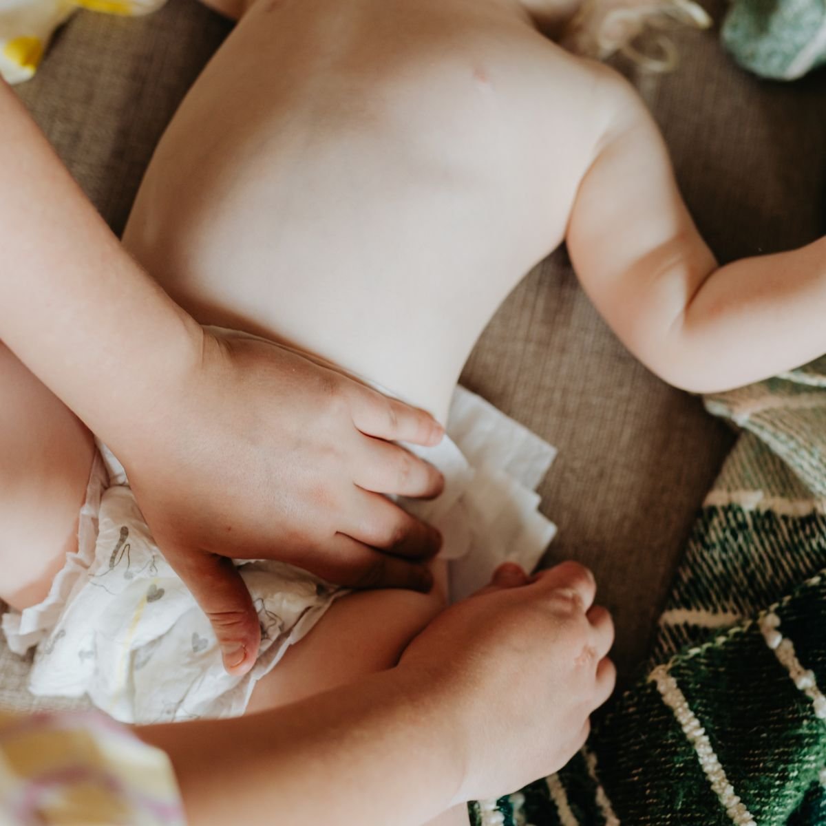 Mother's hands gently caring for newborn baby during diaper change showing invisible caregiving work Image caption: The countless moments of responsive caregiving that perfectionism doesn't count as "accomplishment."