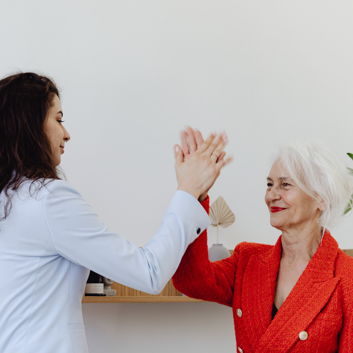 Two women sharing a warm, celebratory moment with a high five, representing the difference between genuine kindness chosen freely and people pleasing driven by anxiety, a key distinction explored in ADHD-informed counselling.