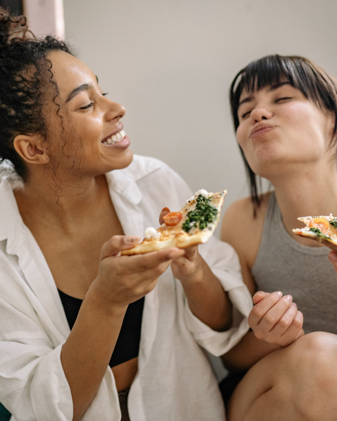 Two women sharing pizza and laughing together, representing how women with ADHD may over-give or people-please in friendships to maintain connection.