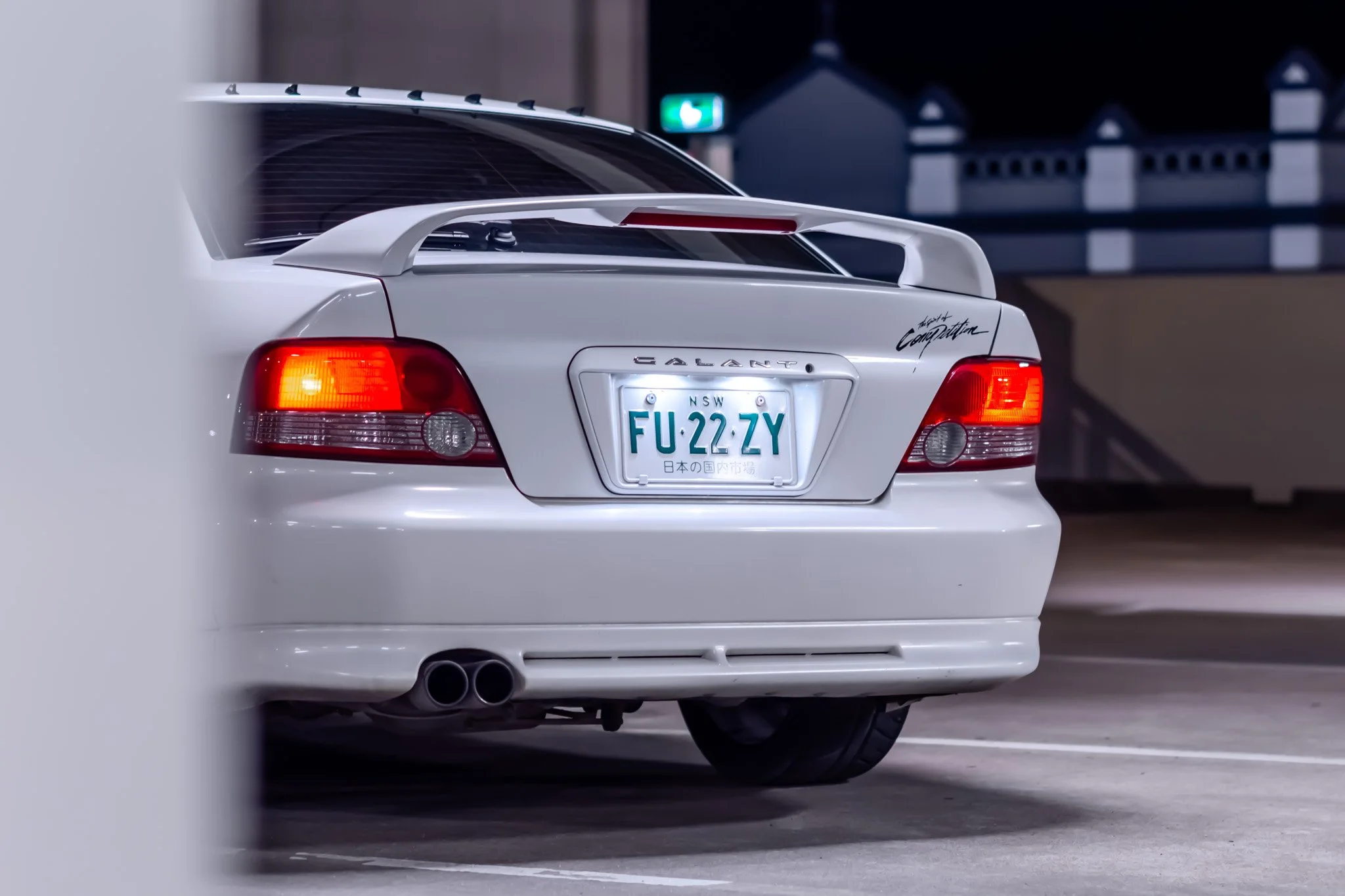 Rear view of a white car parked in a parking garage with a license plate from New South Wales, Australia.