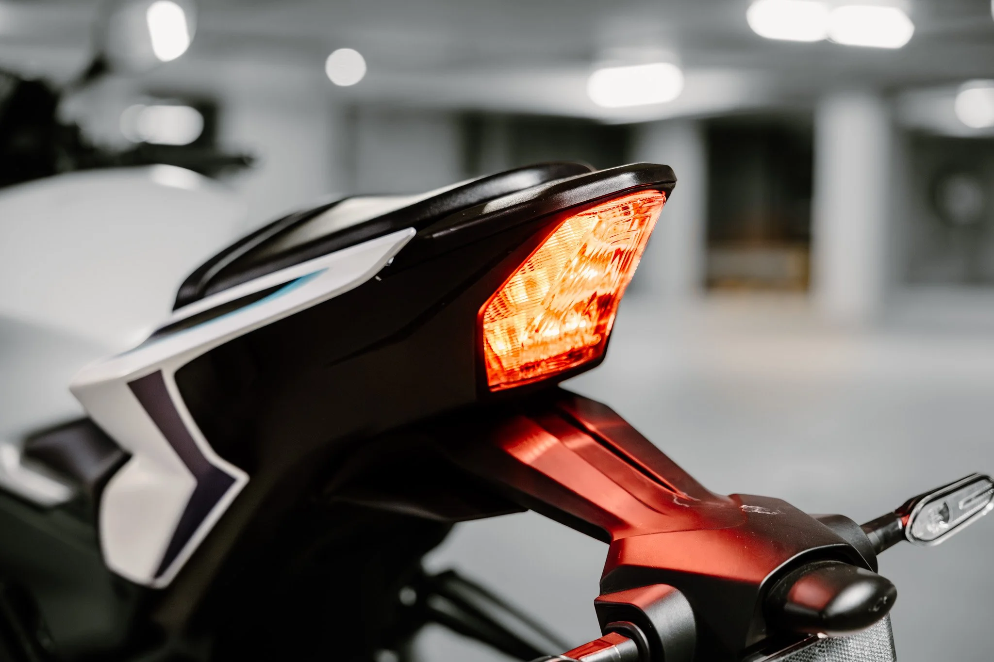 Close-up of a motorcycle tail light with a blurred indoor parking garage background.