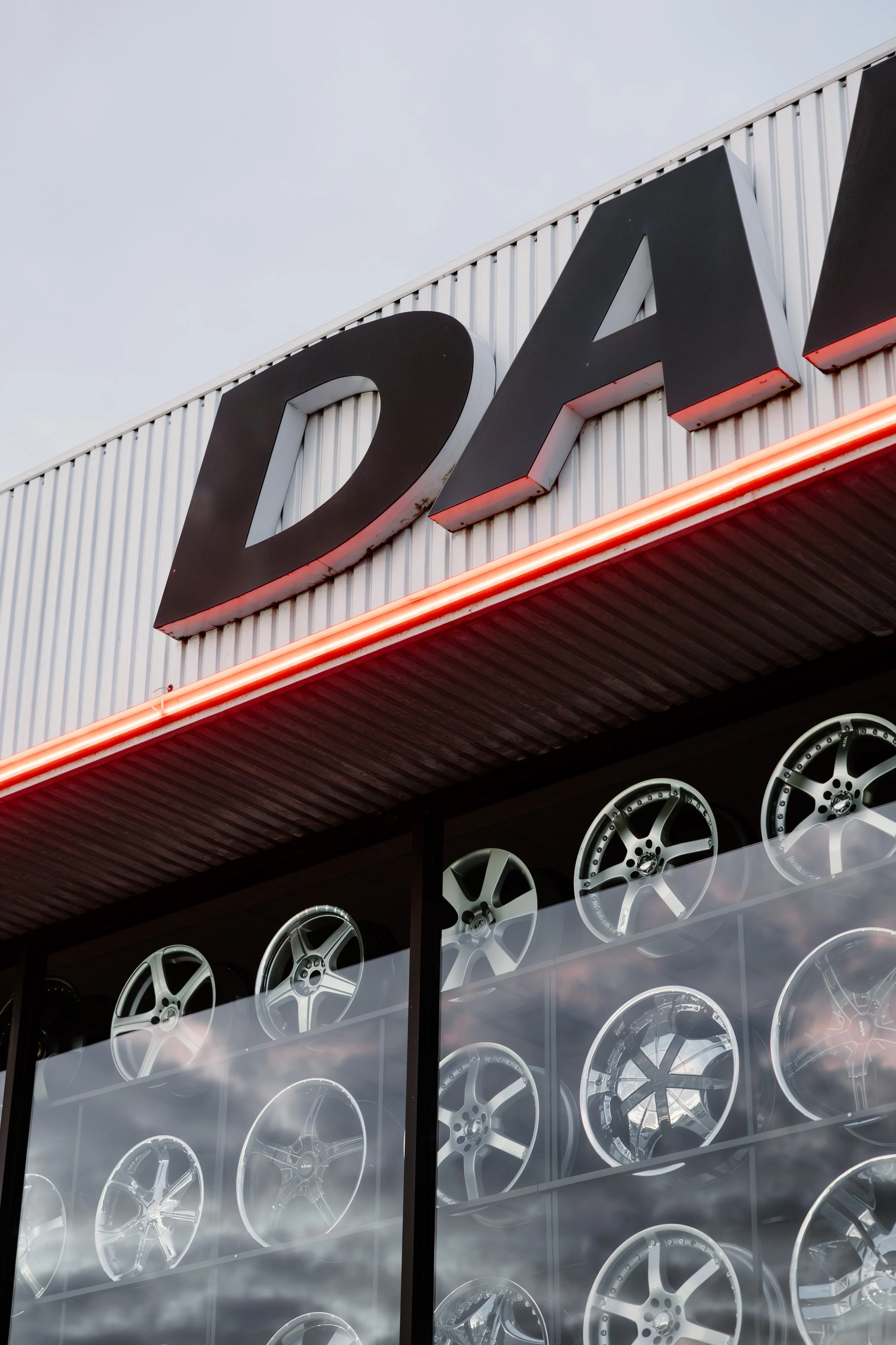 Close-up of a car dealership storefront with large black letters 'Q' and 'A' on the facade, displaying various car wheels in the window below.