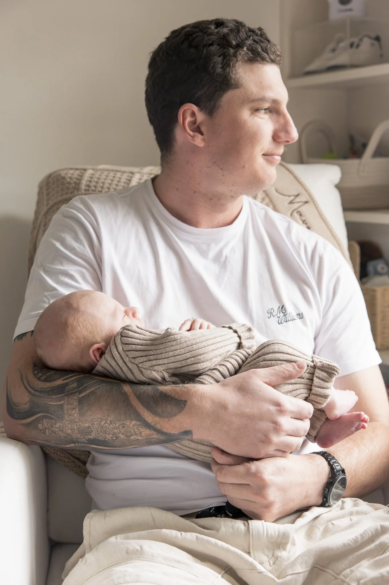 A man holding a baby while sitting on a white couch in a room with a shelf and some items in the background.