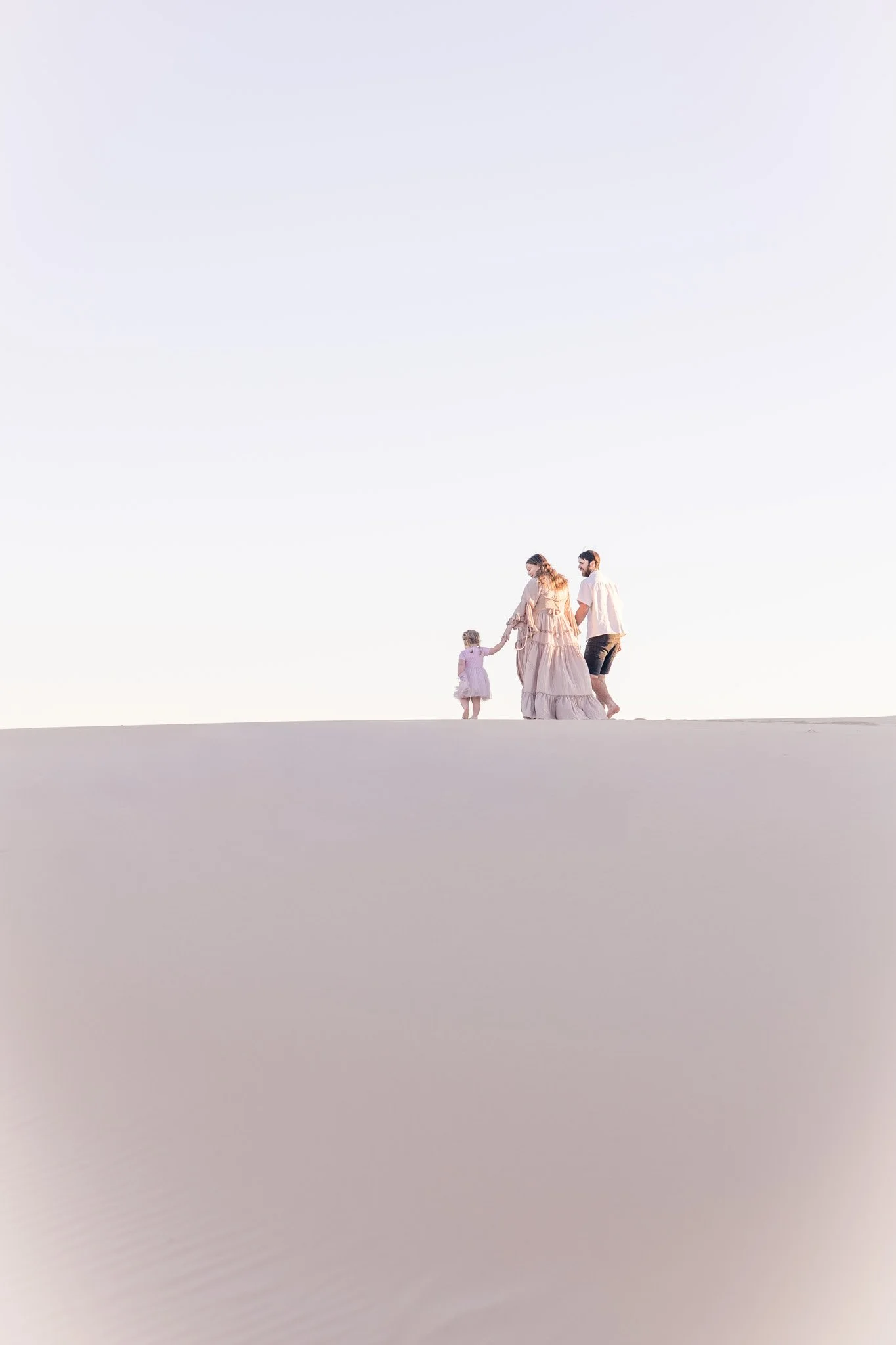 Family of four walking on the beach, holding hands, under a clear sky.