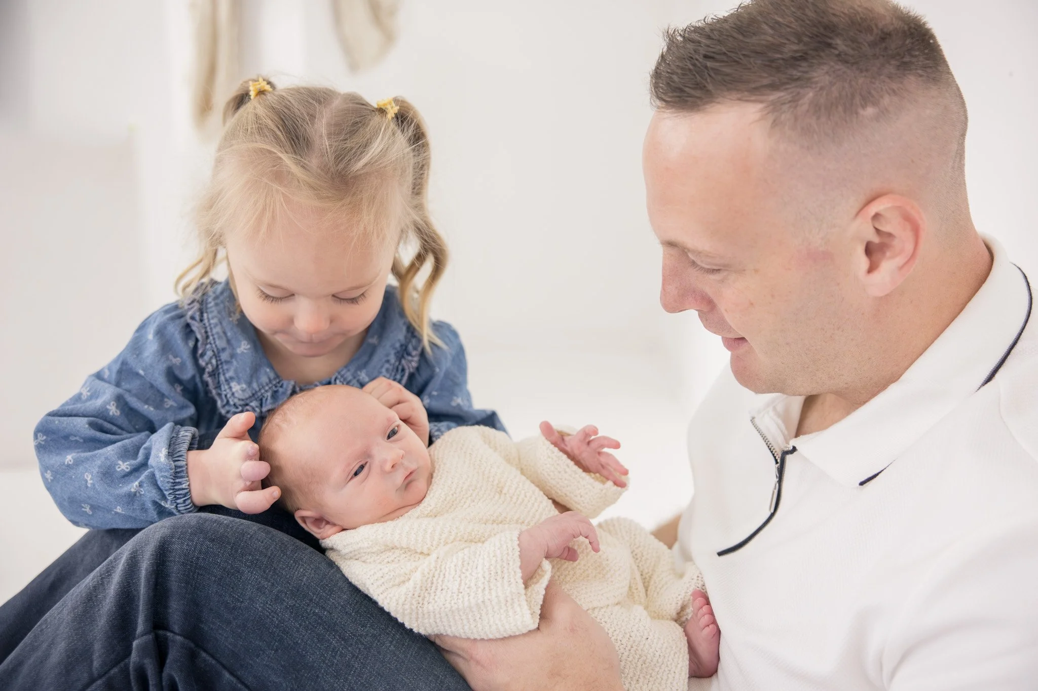 A man holding a newborn baby, with a young girl looking at the baby, all in a bright room.