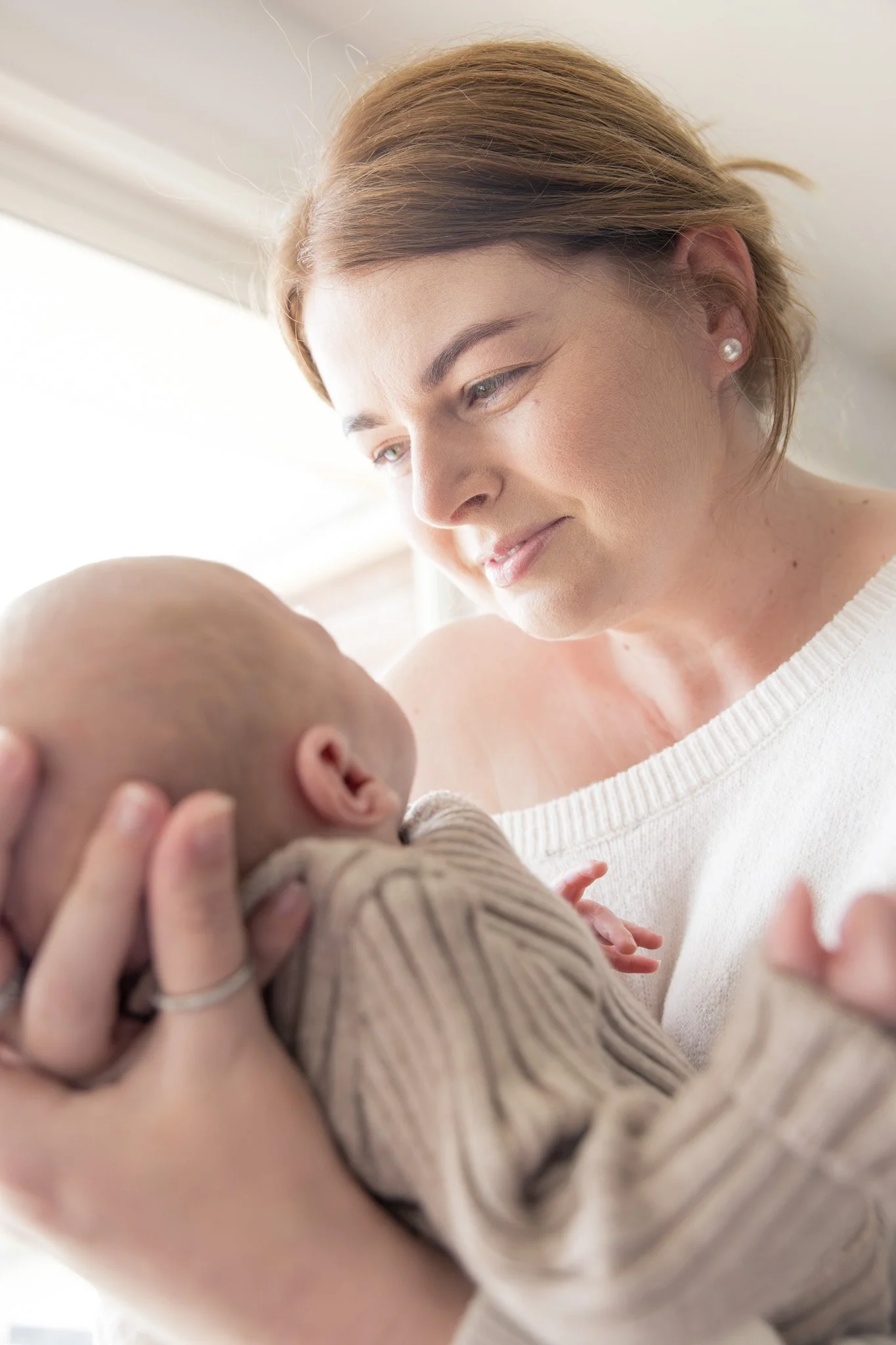 A woman holding a baby close to her chest, smiling and gazing at the baby in a bright, softly lit room.