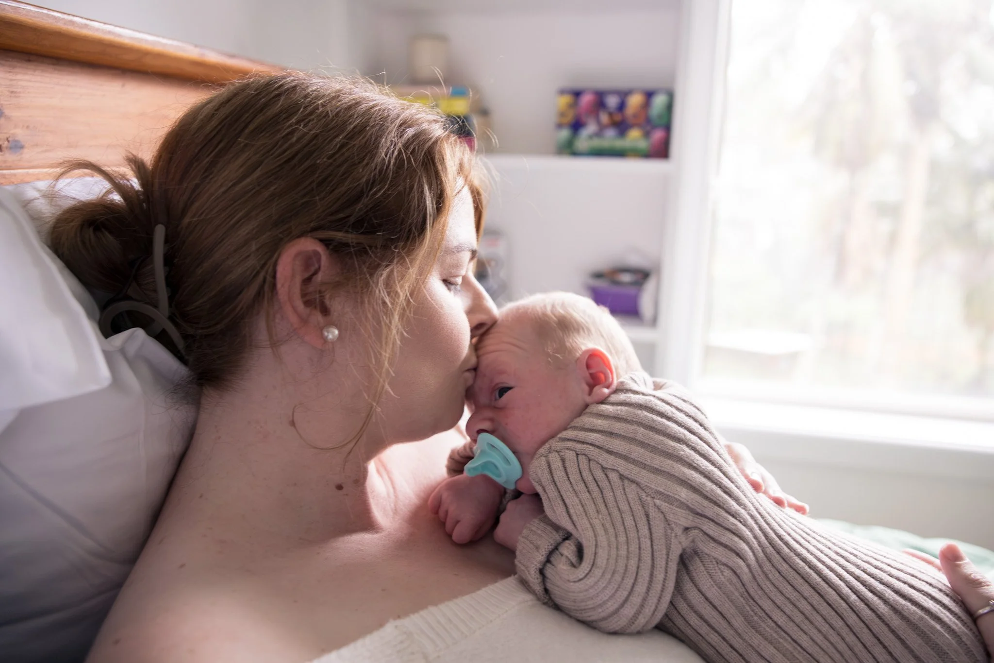 A woman lying in a hospital bed, hugging and kissing a newborn baby.