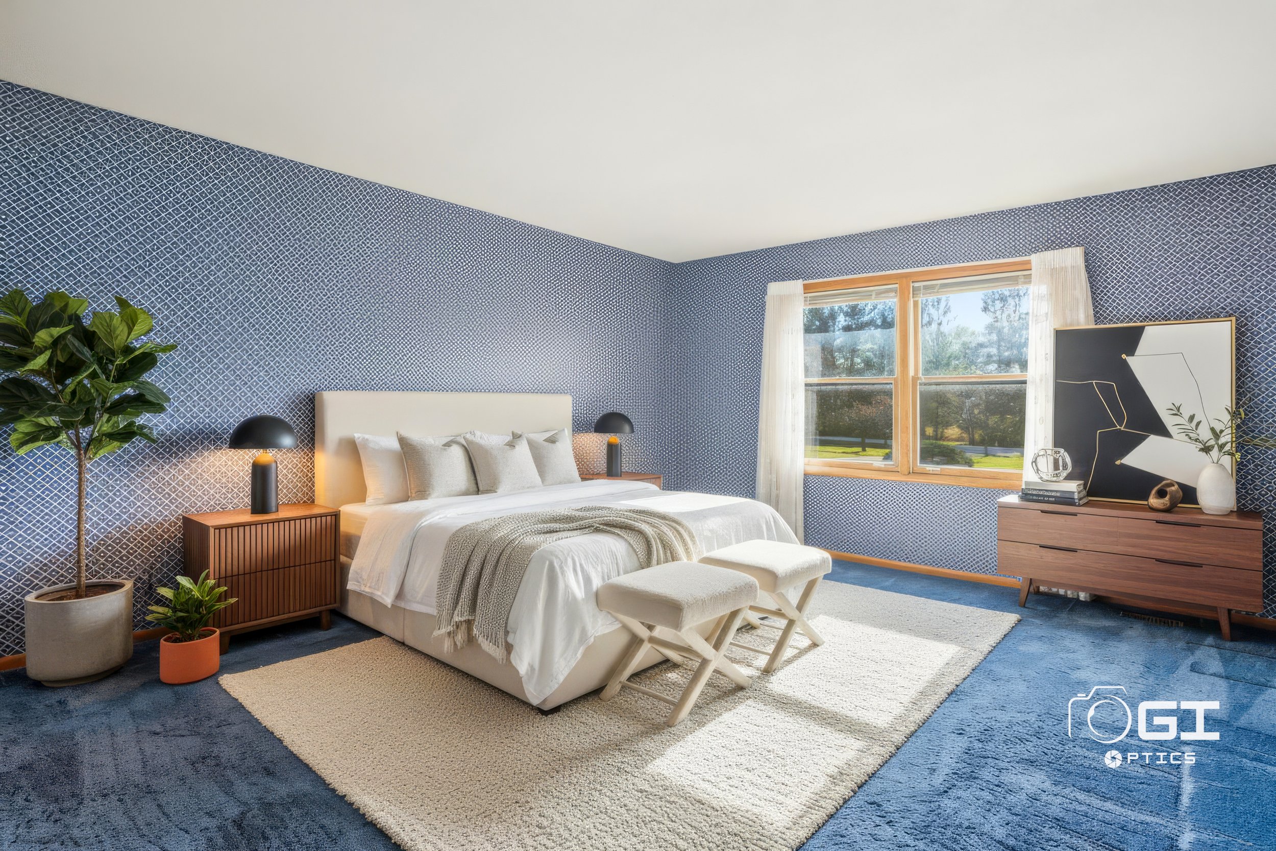 A bedroom with blue patterned walls, a window with white curtains, a beige bed with white and gray pillows, a white bench at the foot of the bed, a wooden nightstand with lamps, a wooden dresser with decorative objects and artwork, a potted plant, an