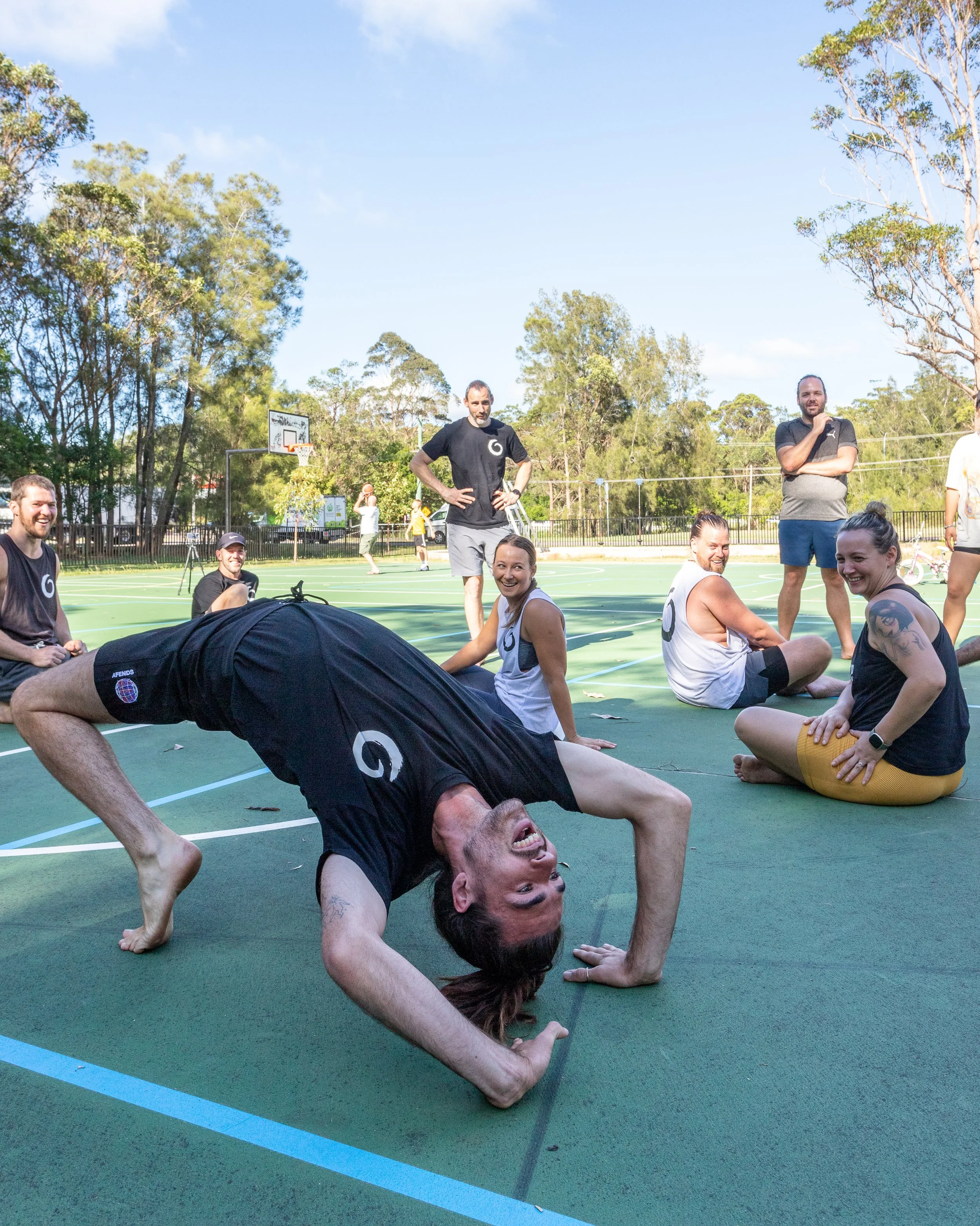 Group movement session on an outdoor court, combining playful inversion and community practice.