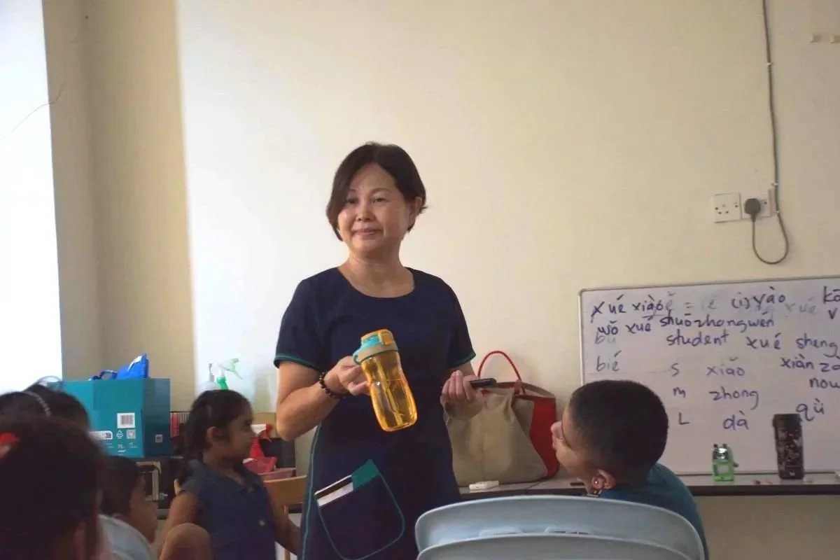 A Mandarin language teacher holding a water bottle while teaching children Mandarin in a classroom in Banting