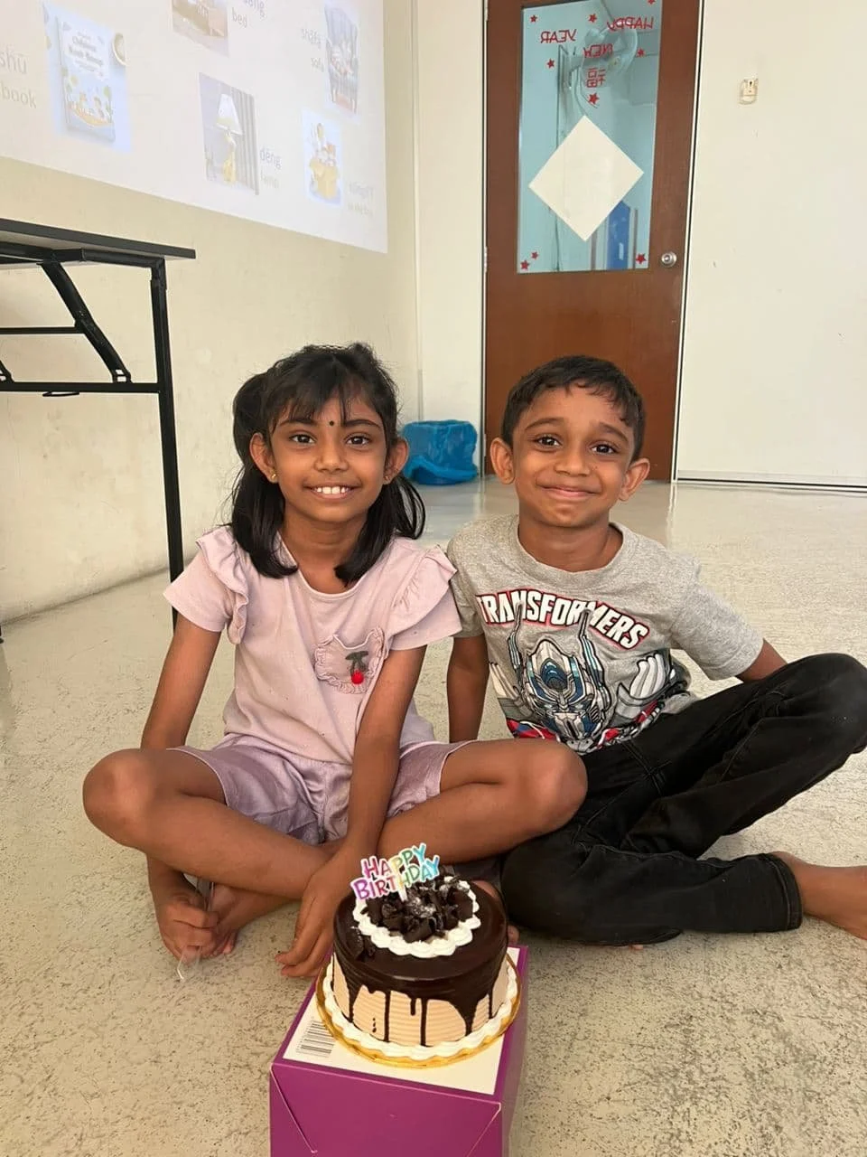 Two children sitting down and smiling in a classroom in Banting