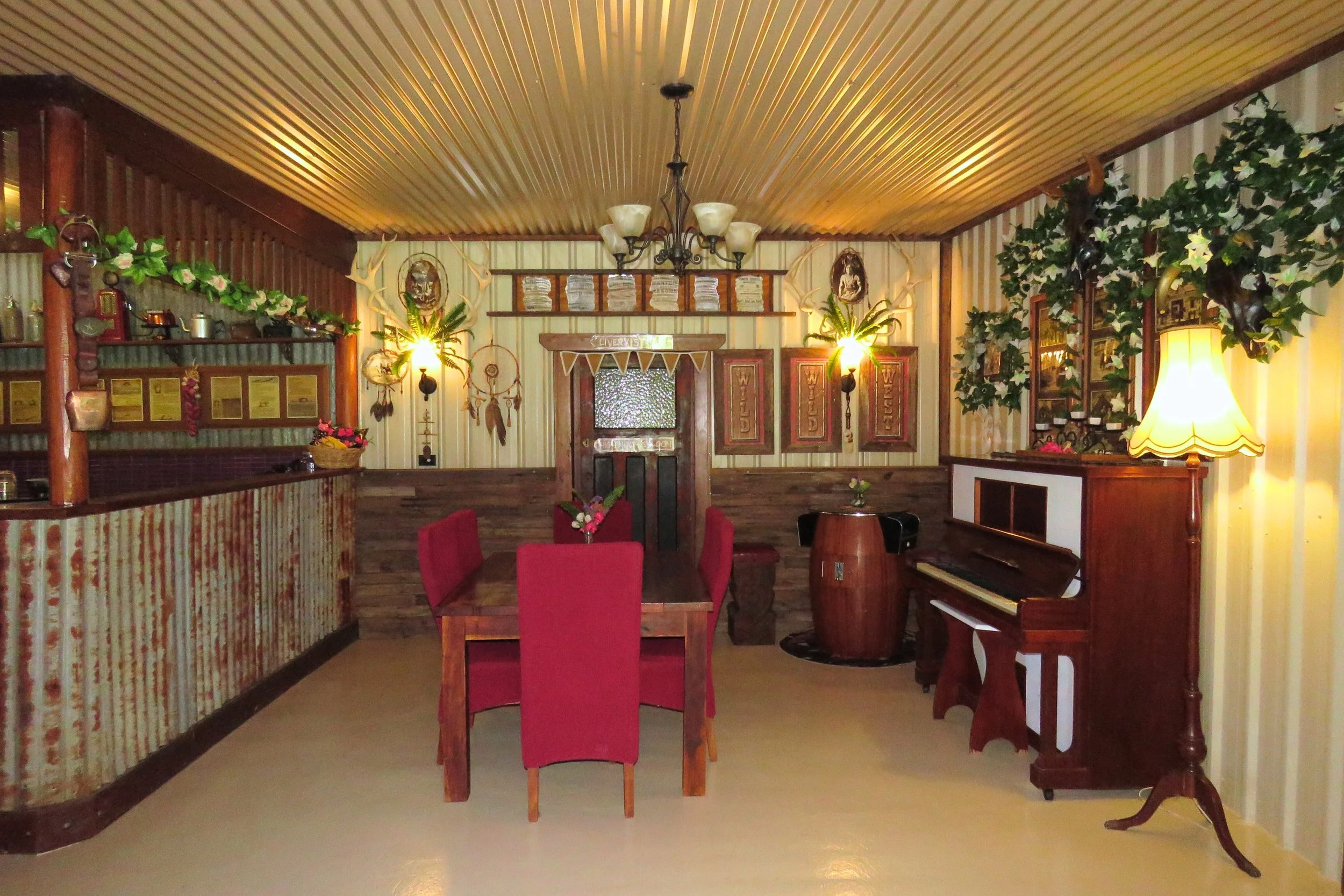 Cozy dining room with a wooden table and red chairs, vintage piano, decorative wall art, porch wall lighting, and plants.