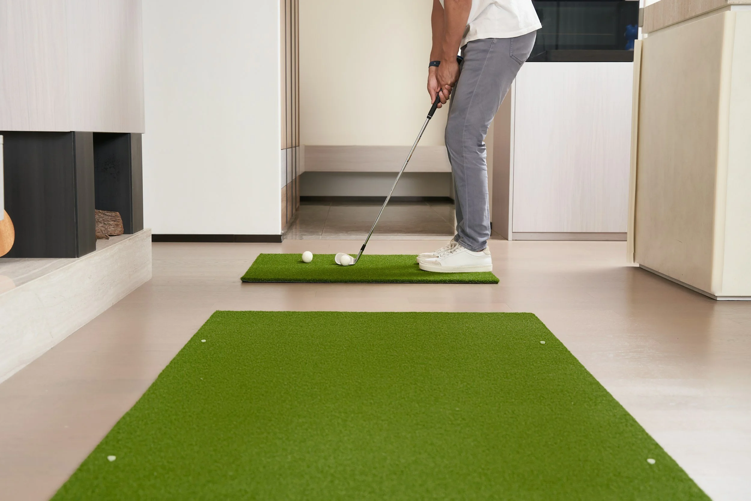 Person playing indoor mini golf, preparing to hit a golf ball on a green mat.