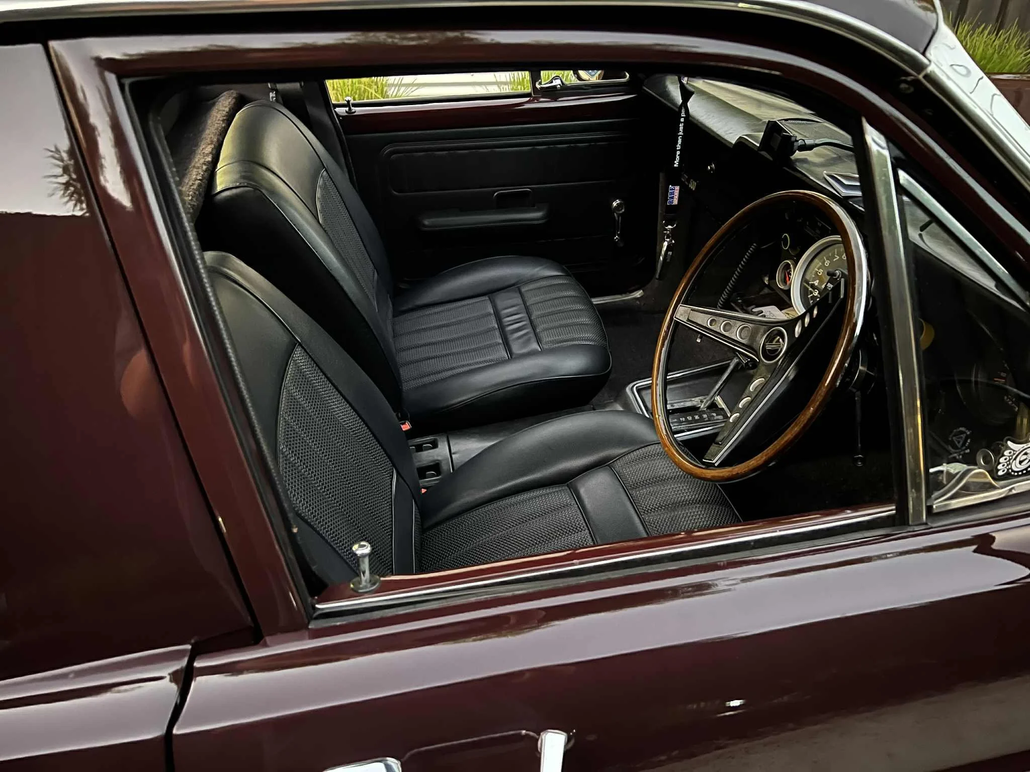Interior of a vintage car showing black leather seats, wooden steering wheel, and dashboard with classic gauges.