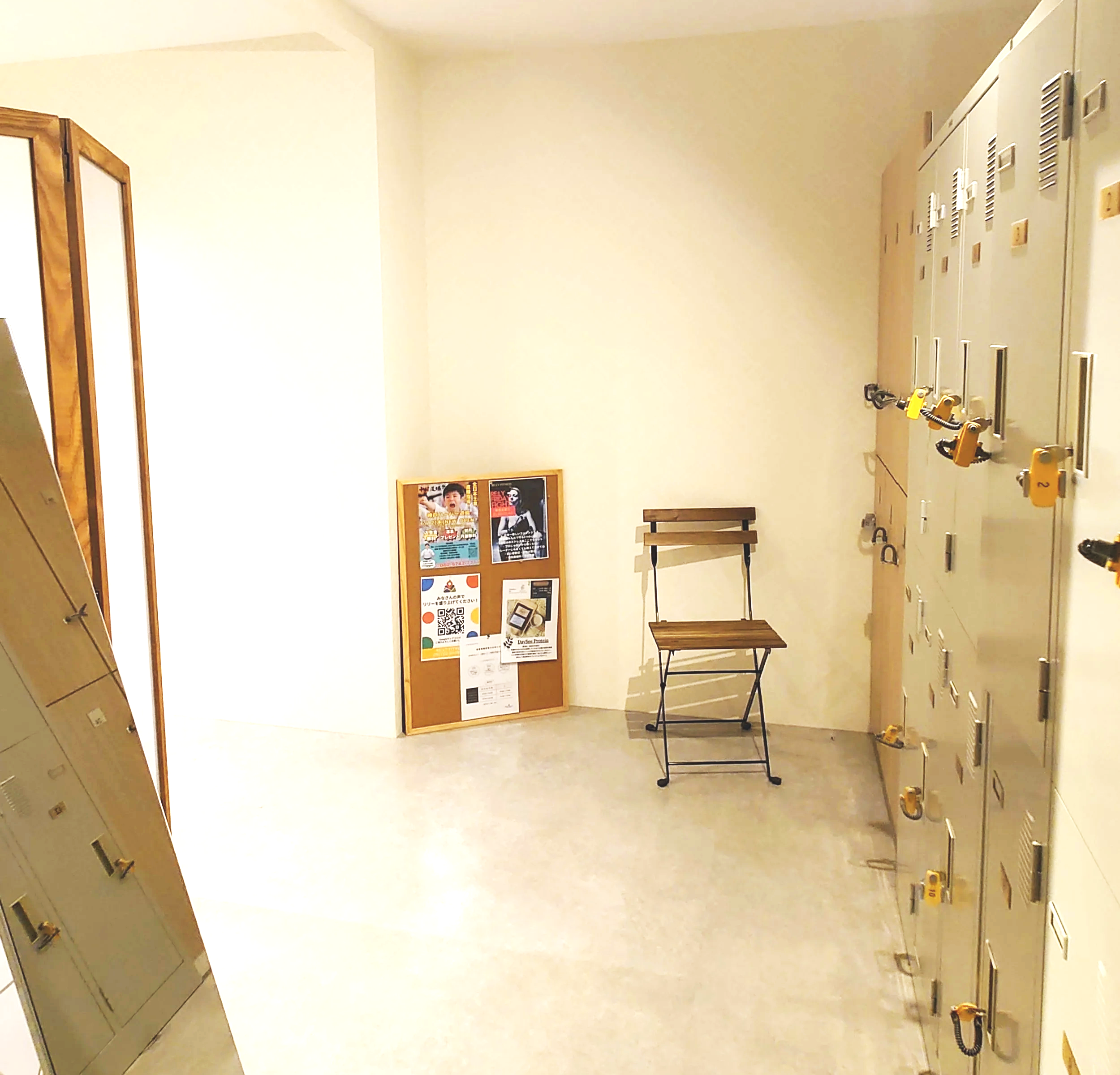 ロッカーのある部屋で、壁に掲示板と折りたたみ椅子が置かれている。
