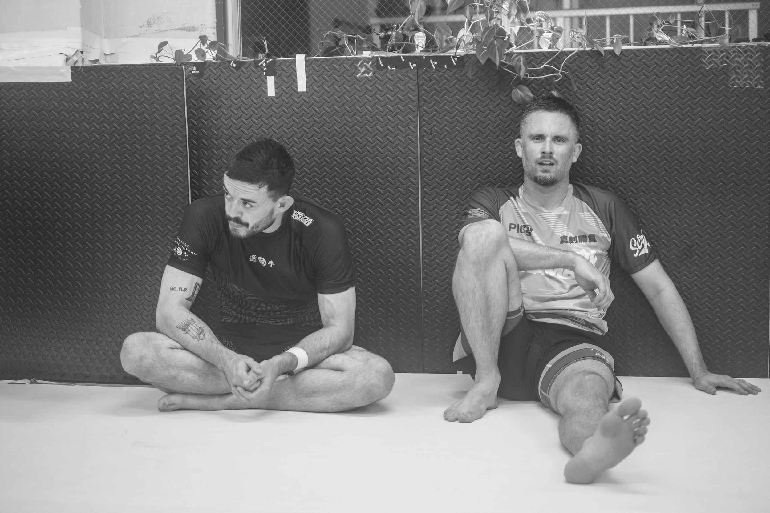 二人の男性が格闘技のトレーニング後に座って休憩している。Billy Hooker and Matt Benyon of SCRAMBLE BRAND chilling after Jiu-Jitsu training in Osaka. BADDIES JIU-JITSU
