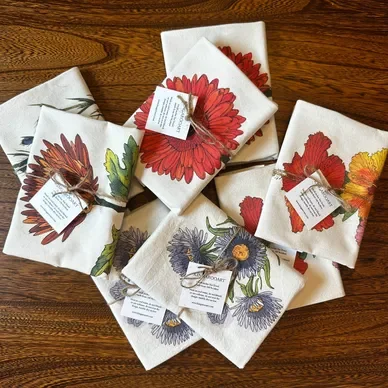 Several folded cloth napkins with floral patterns, tied with natural twine, spread out on a wooden surface.