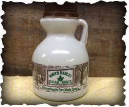 A white half pint of maple syrup with a brown lid, labeled 'North Hadley Sugar Shack' and featuring a picture of trees on the front.