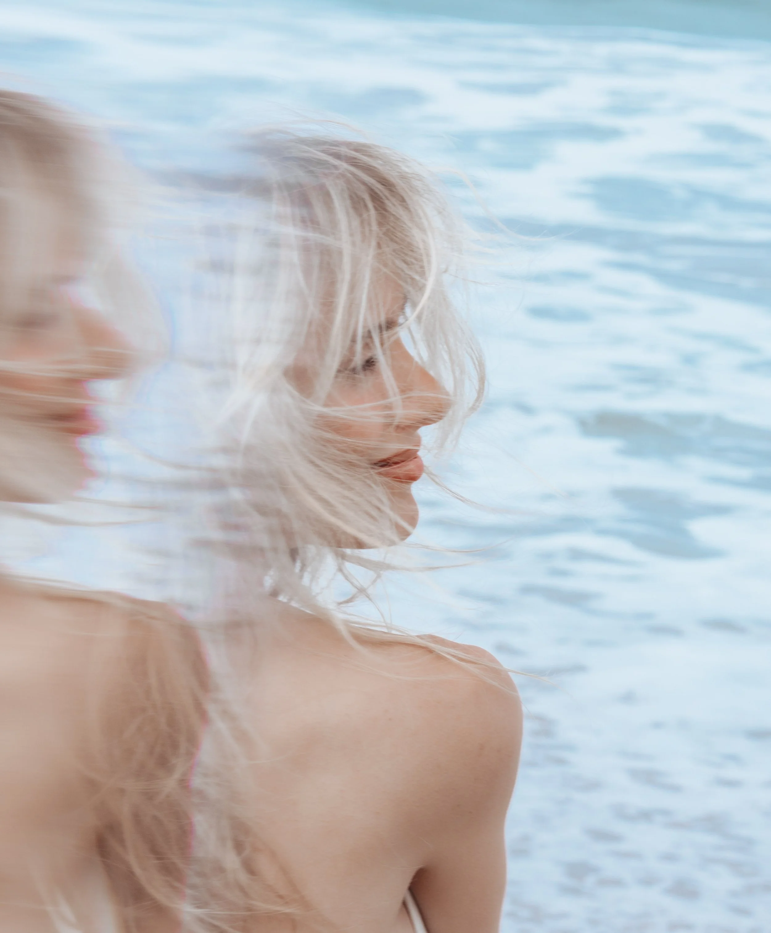 A woman with long blonde hair at the beach, with the ocean in the background.