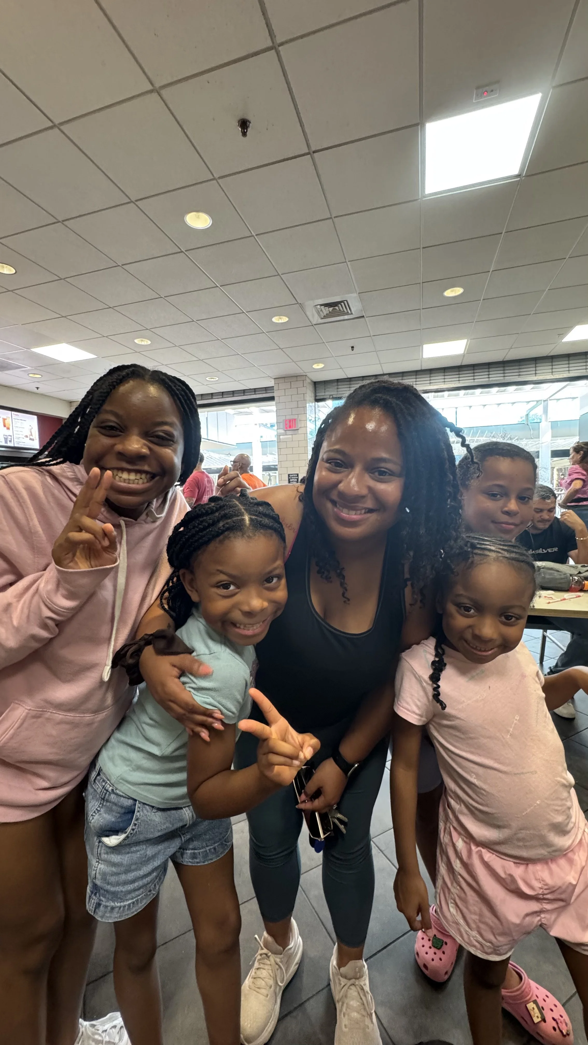 A group of smiling people, including women and children, posing together inside a fast-food restaurant, with some giving peace signs.