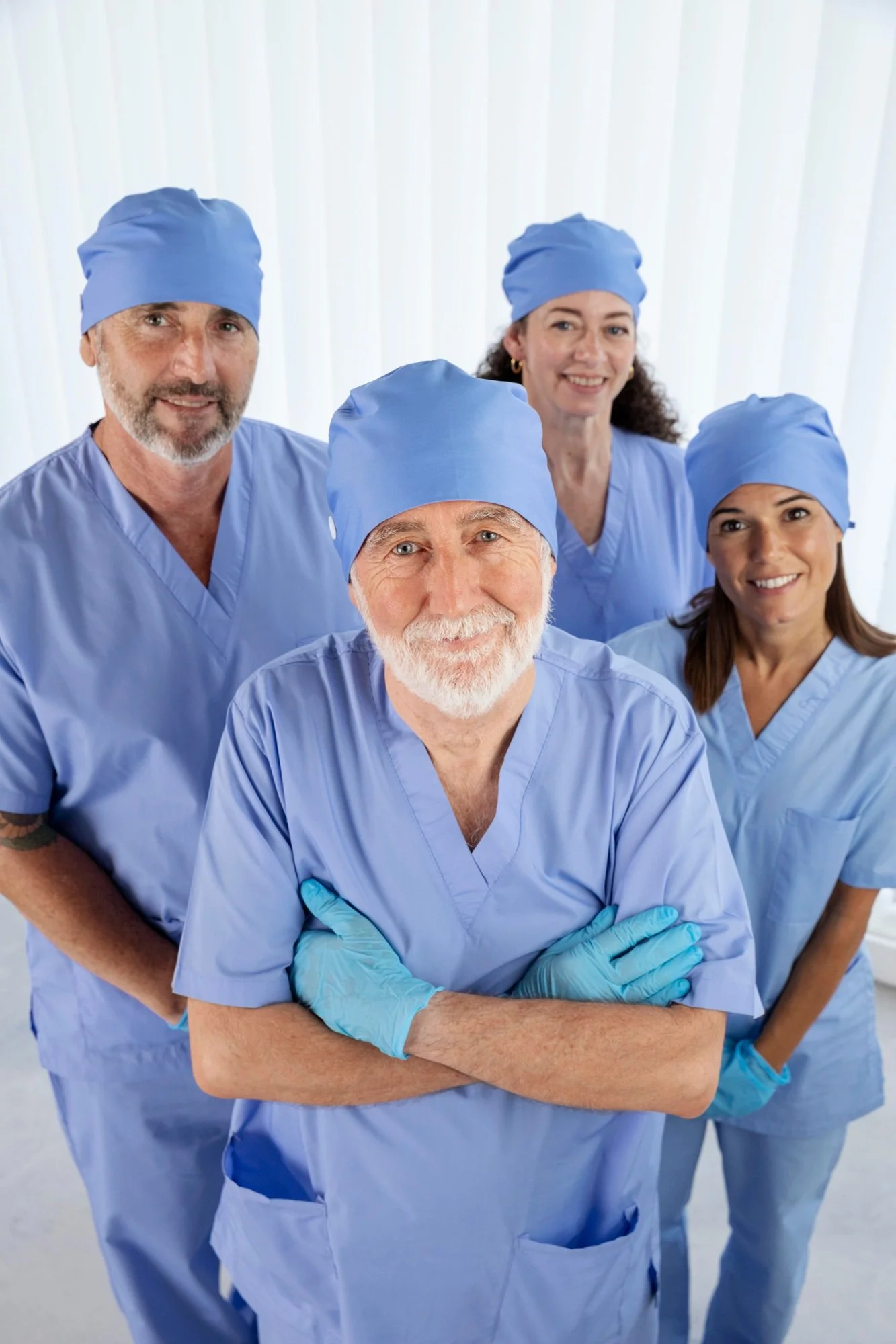 Group of four diverse medical professionals in scrubs and surgical caps posing confidently in a clinical setting.