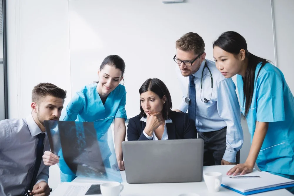 Medical team reviewing X-ray images on a laptop in a hospital conference room.