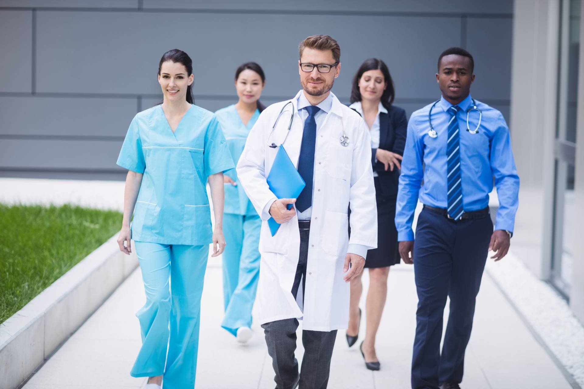 A diverse group of healthcare professionals, including doctors and nurses, walking outside a modern medical facility.