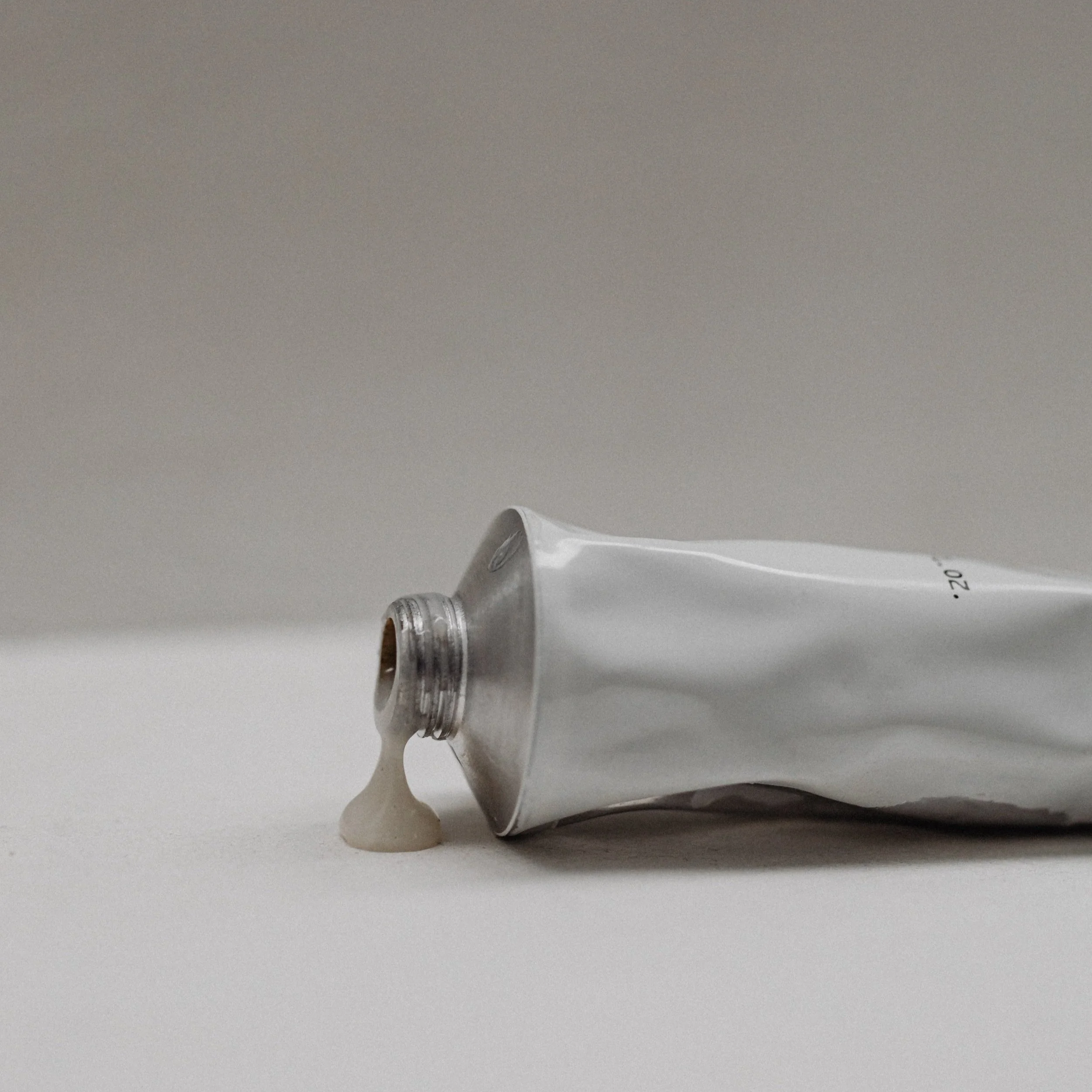 A tube of white cream with some cream spilled on white surface.